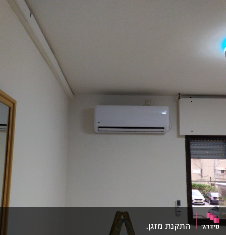 מזגן מותקן על קיר ליד חלון עם שלט רחוק